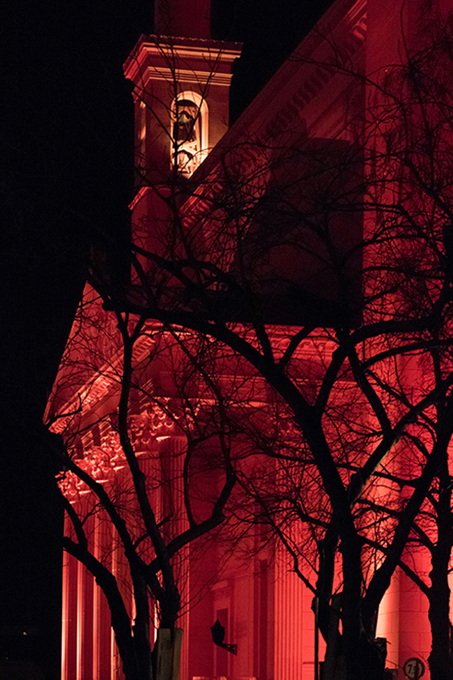 schwarzer Baum vor rot beleuchtetem Gebäude